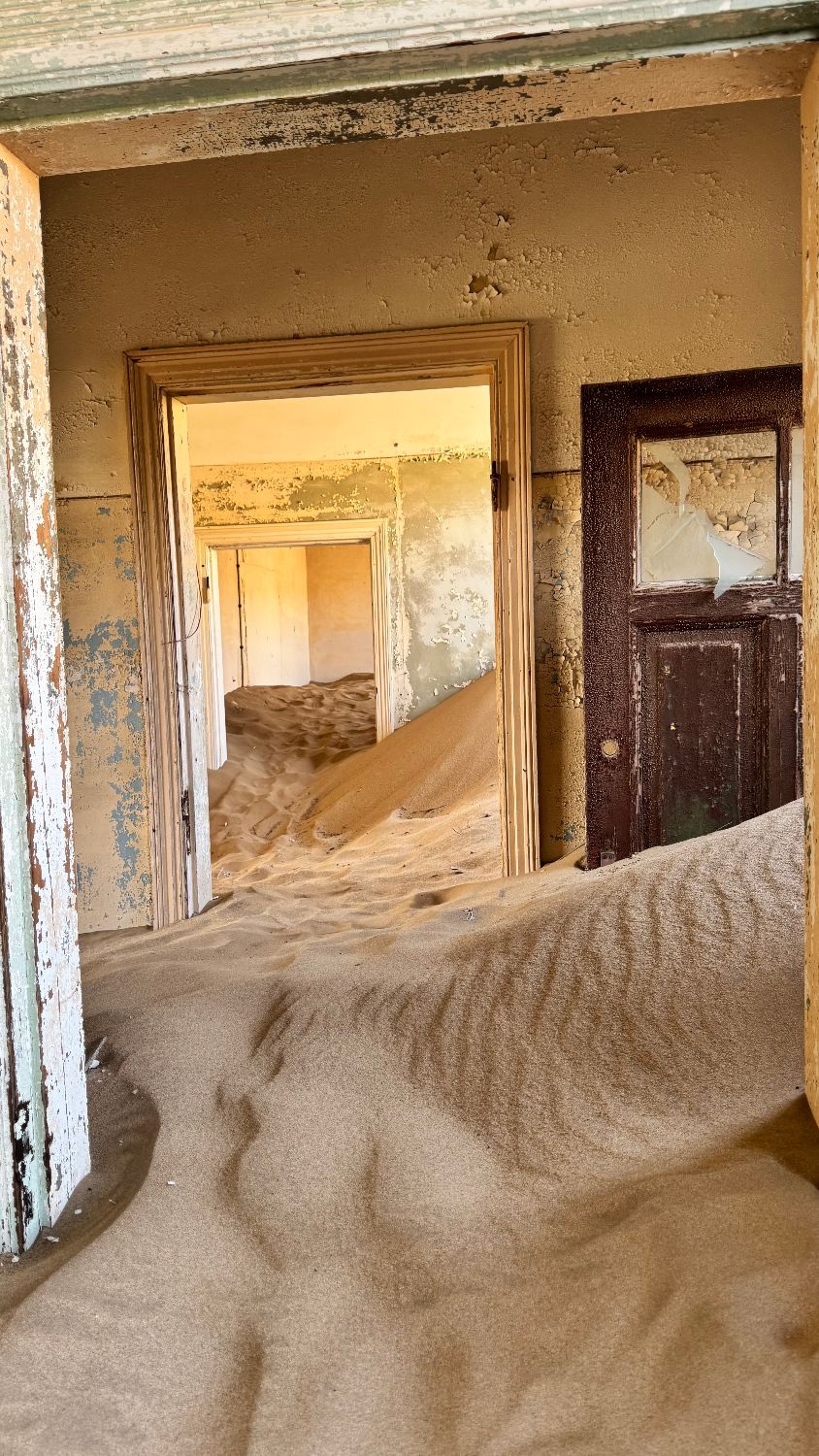 Sand drifting through three doorways at Kolmanskop